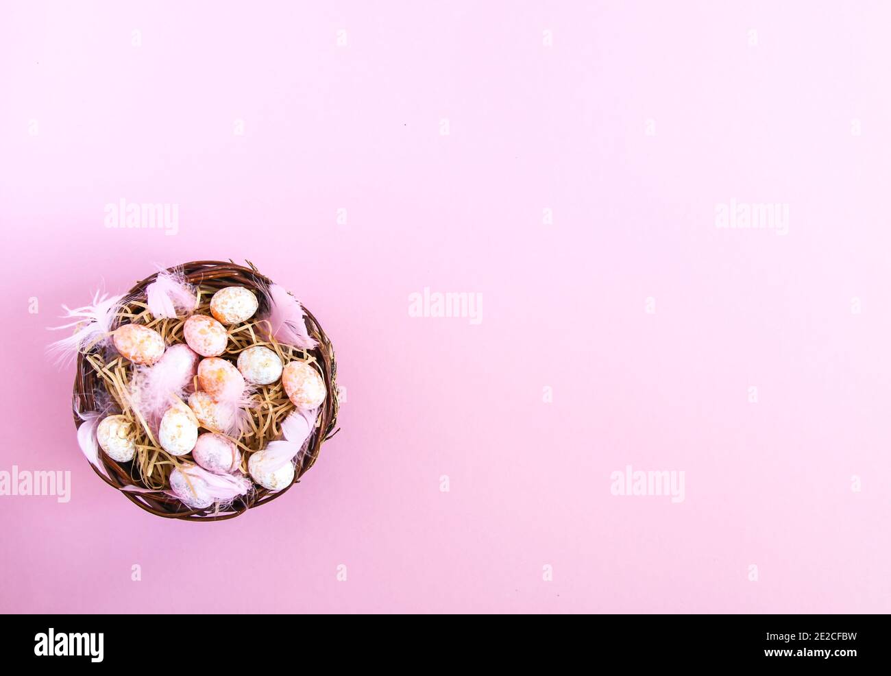 Composizione pasquale con decor tradizionale. Piccole uova colorate decorative e piume morbide in un cesto di vimini su sfondo rosa chiaro. Foto Stock