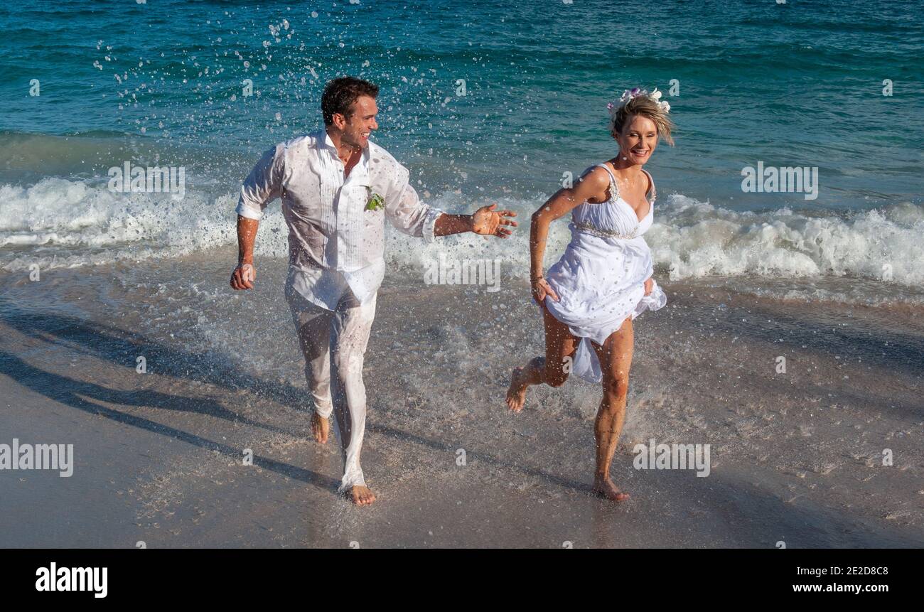 Le coppie appena sposate celebrano il loro matrimonio su una spiaggia dell'isola caraibica di Mustique. Mano in mano che si spruzzi nel surf e spazzare l'abito. Foto Stock