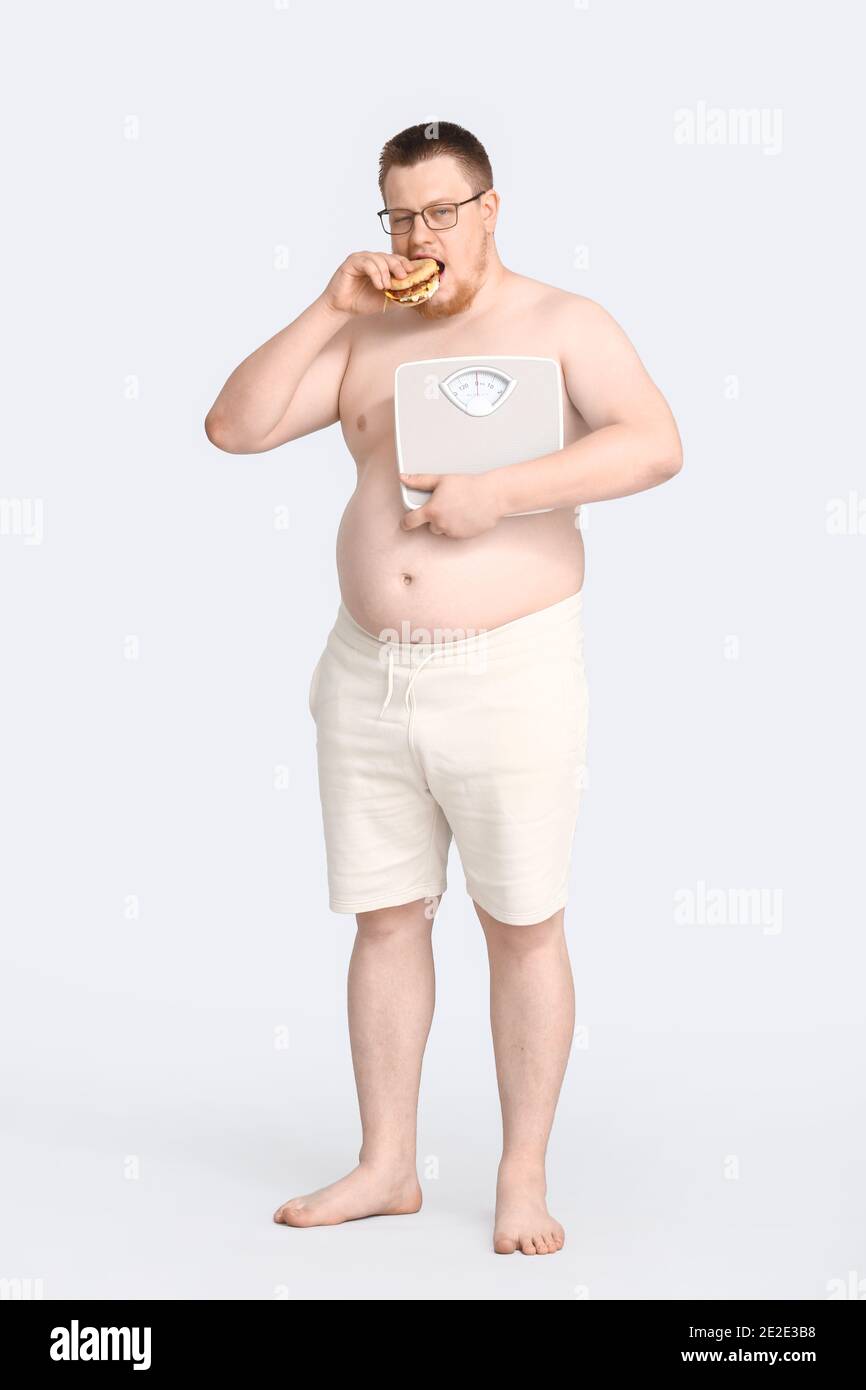 Uomo sovrappeso con scale mangiare hamburger malsano su sfondo grigio.  Concetto di perdita di peso Foto stock - Alamy