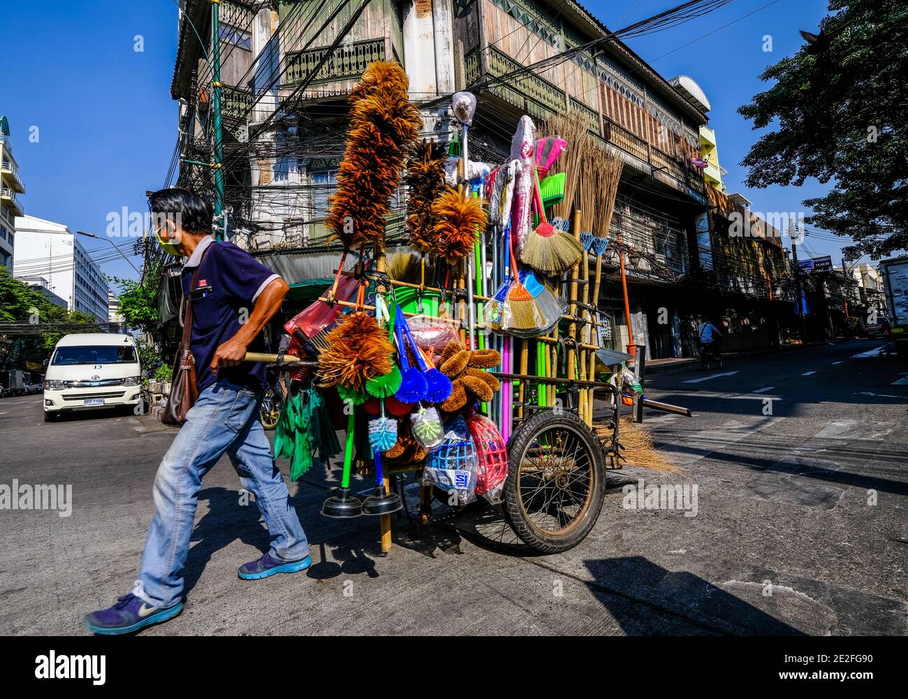 Un venditore di spazzole mobili trasporta i suoi articoli lungo una strada nella zona di Talat noi di Bangkok, Thailandia Foto Stock