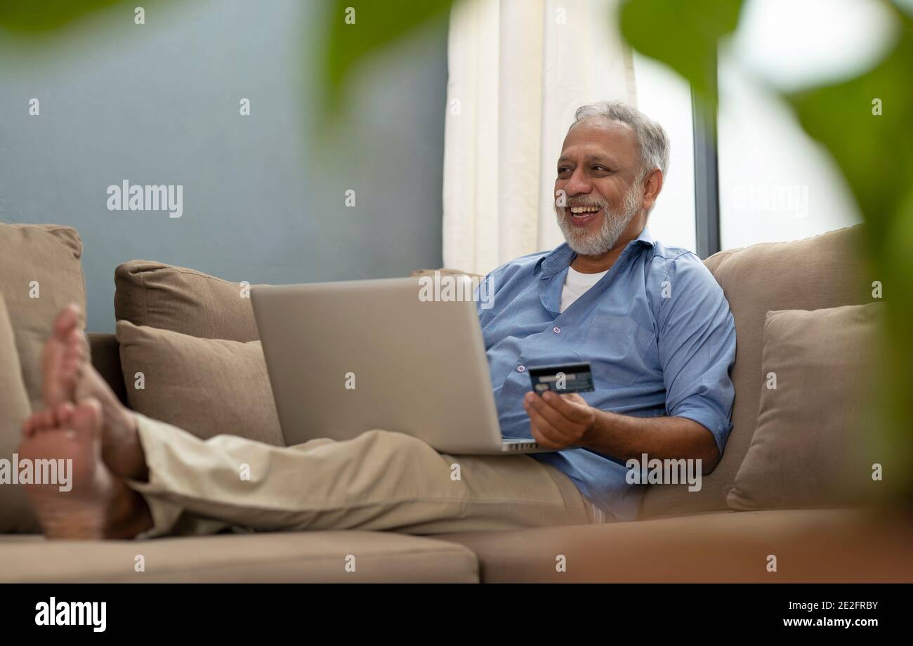 UN UOMO ADULTO ANZIANO FELICEMENTE USANDO LA CARTA DI DEBITO PER FARE TRANSAZIONI ONLINE Foto Stock