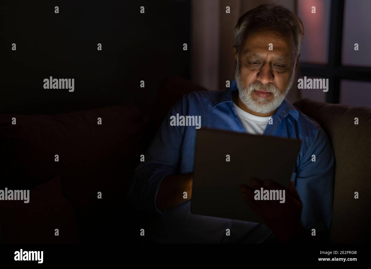 UN ADULTO ANZIANO CHE UTILIZZA UN TABLET DIGITALE DI NOTTE Foto Stock