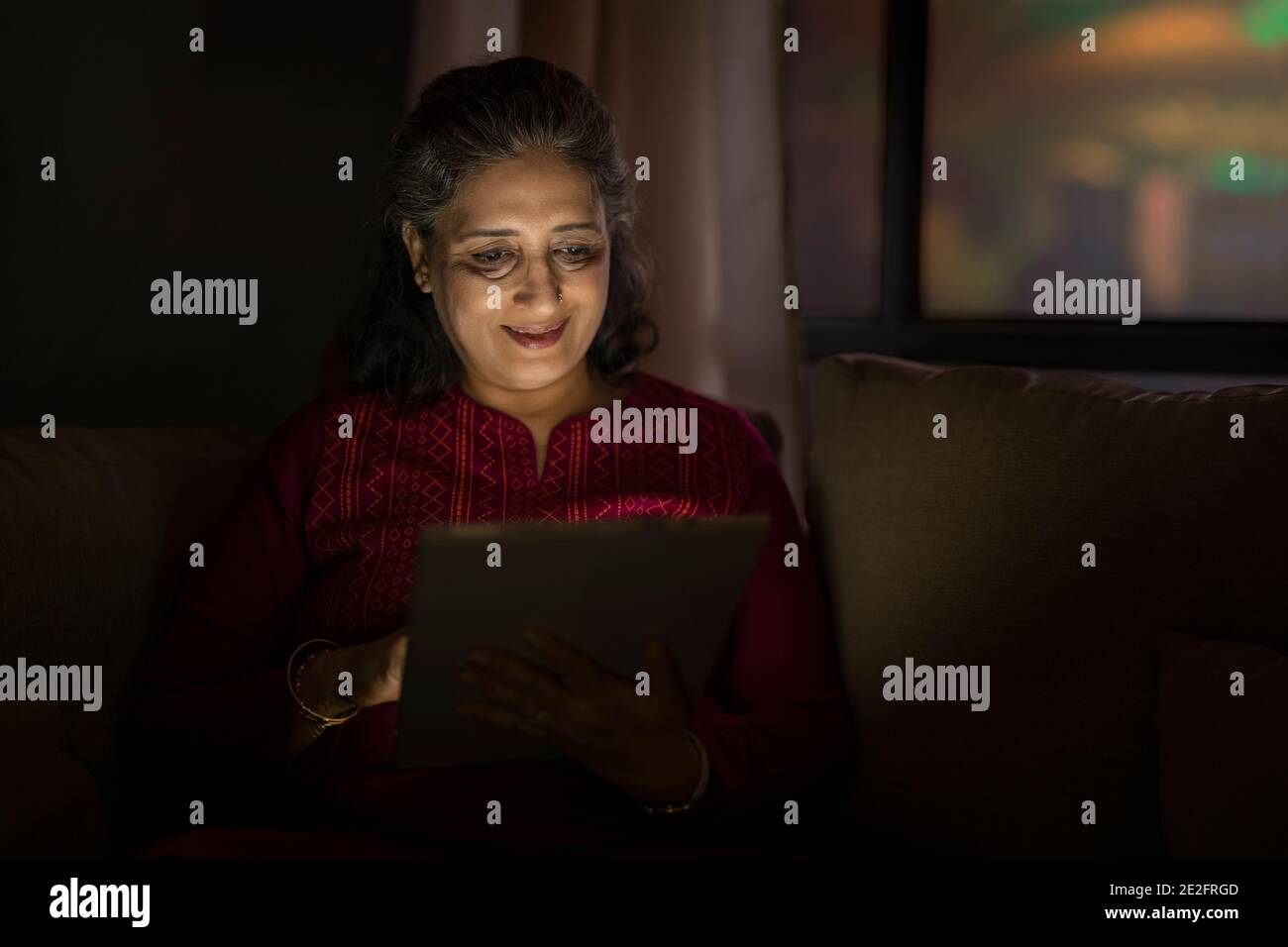 UNA DONNA ANZIANA ADULTA SEDUTA E FELICEMENTE UTILIZZANDO UN TABLET DIGITALE Foto Stock