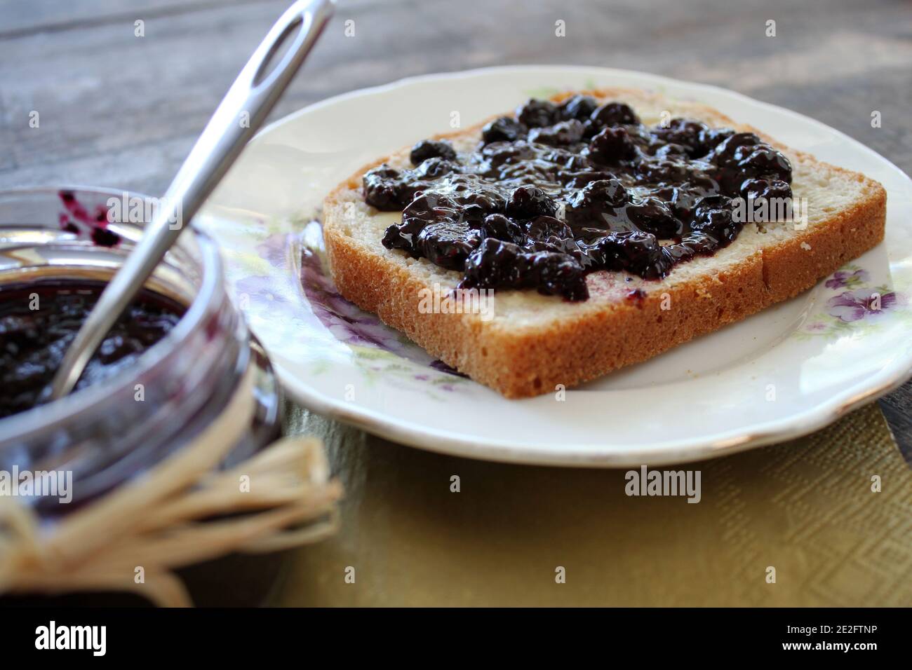 Una fetta fresca di pane con una marmellata di mirtilli spalmata su un tavolo rustico in legno Foto Stock