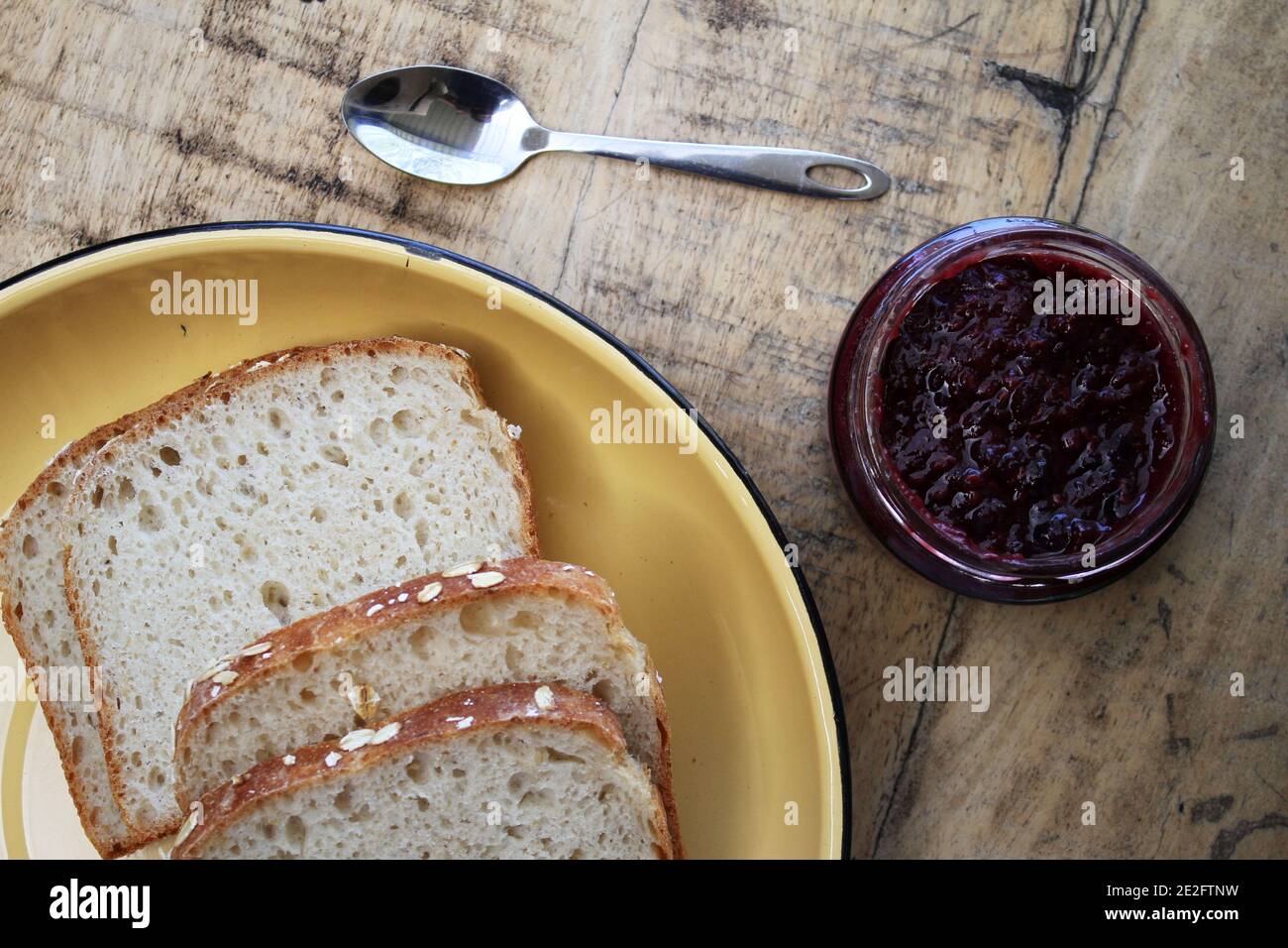 Una marmellata di vasetto accanto ad un piatto di pane e un cucchiaio contro uno sfondo rustico di legno Foto Stock