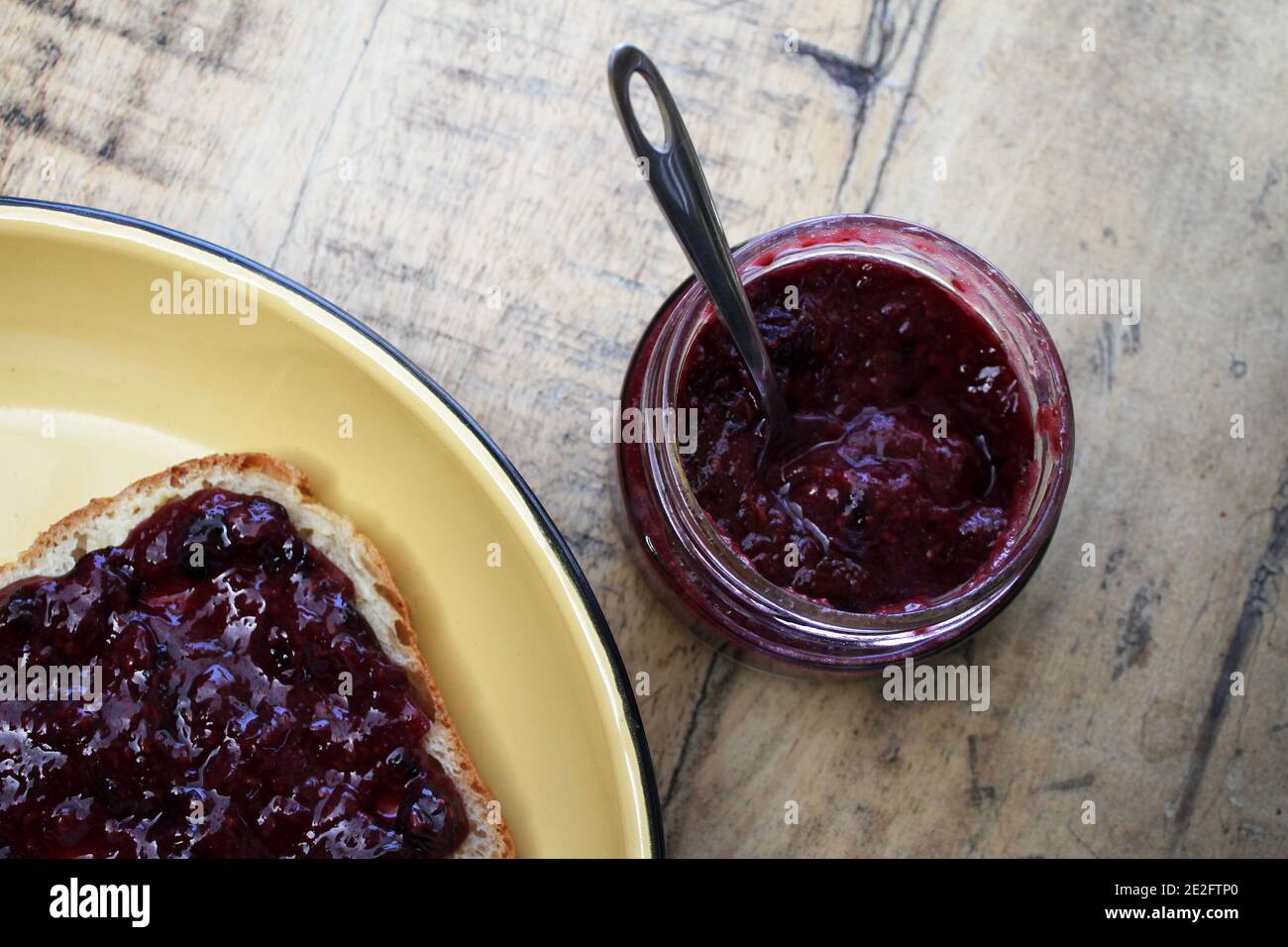 Un vasetto di confettura di lamponi accanto a una fetta di pane sullo sfondo di un tavolo rustico. Foto Stock