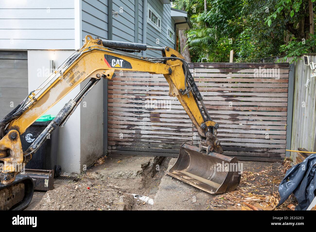 Miniescavatore scavare meccanicamente una trincea per riparare una rottura Tubo di drenaggio, Sydney, Australia Foto Stock