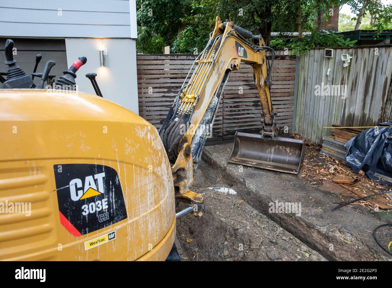 Miniescavatore scavare meccanicamente una trincea per riparare una rottura Tubo di drenaggio, Sydney, Australia Foto Stock