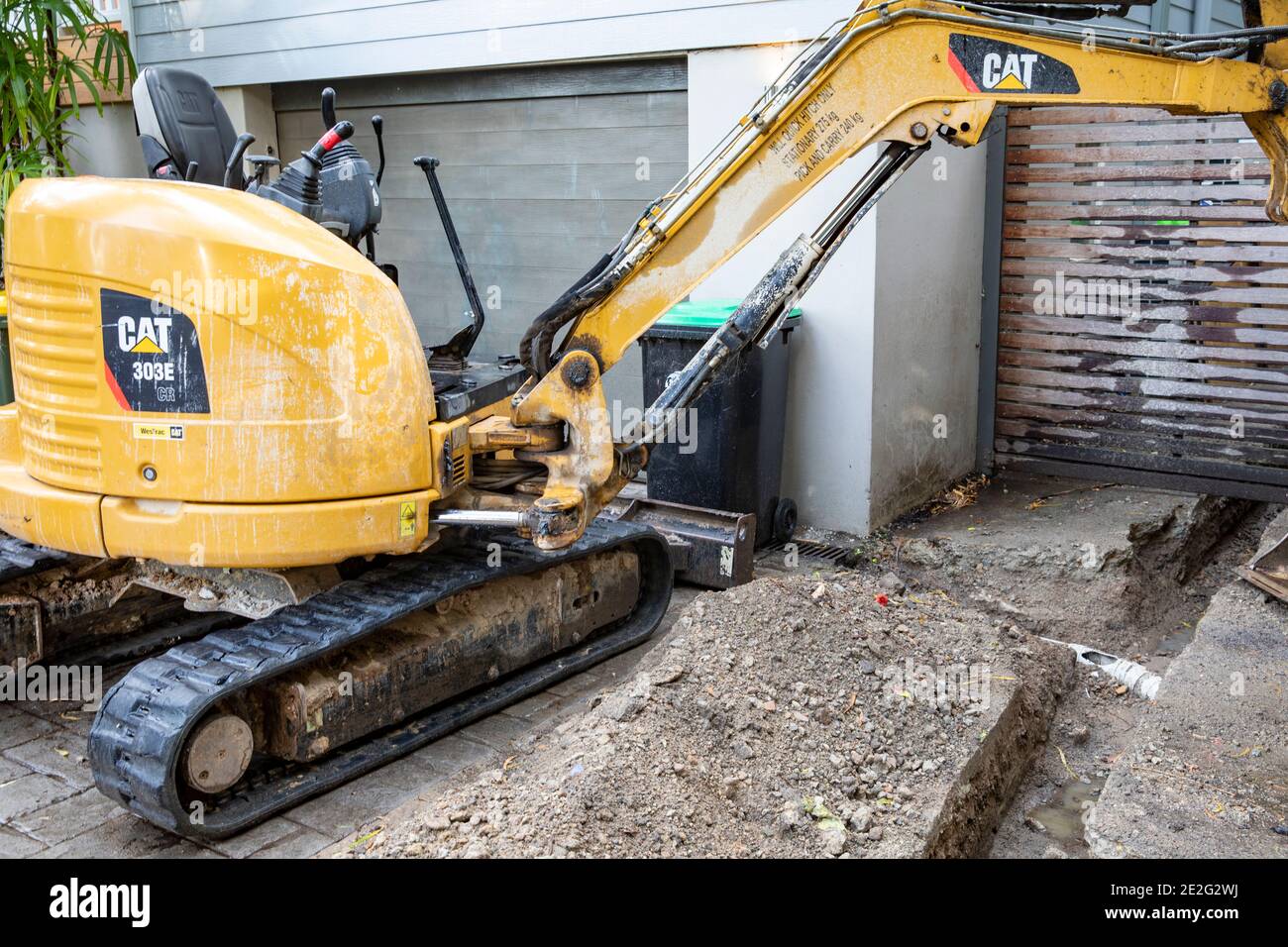 Miniescavatore scavare una trincea per accedere alla riparazione di rotture Tubo di drenaggio delle acque piovane, Sydney, Australia Foto Stock