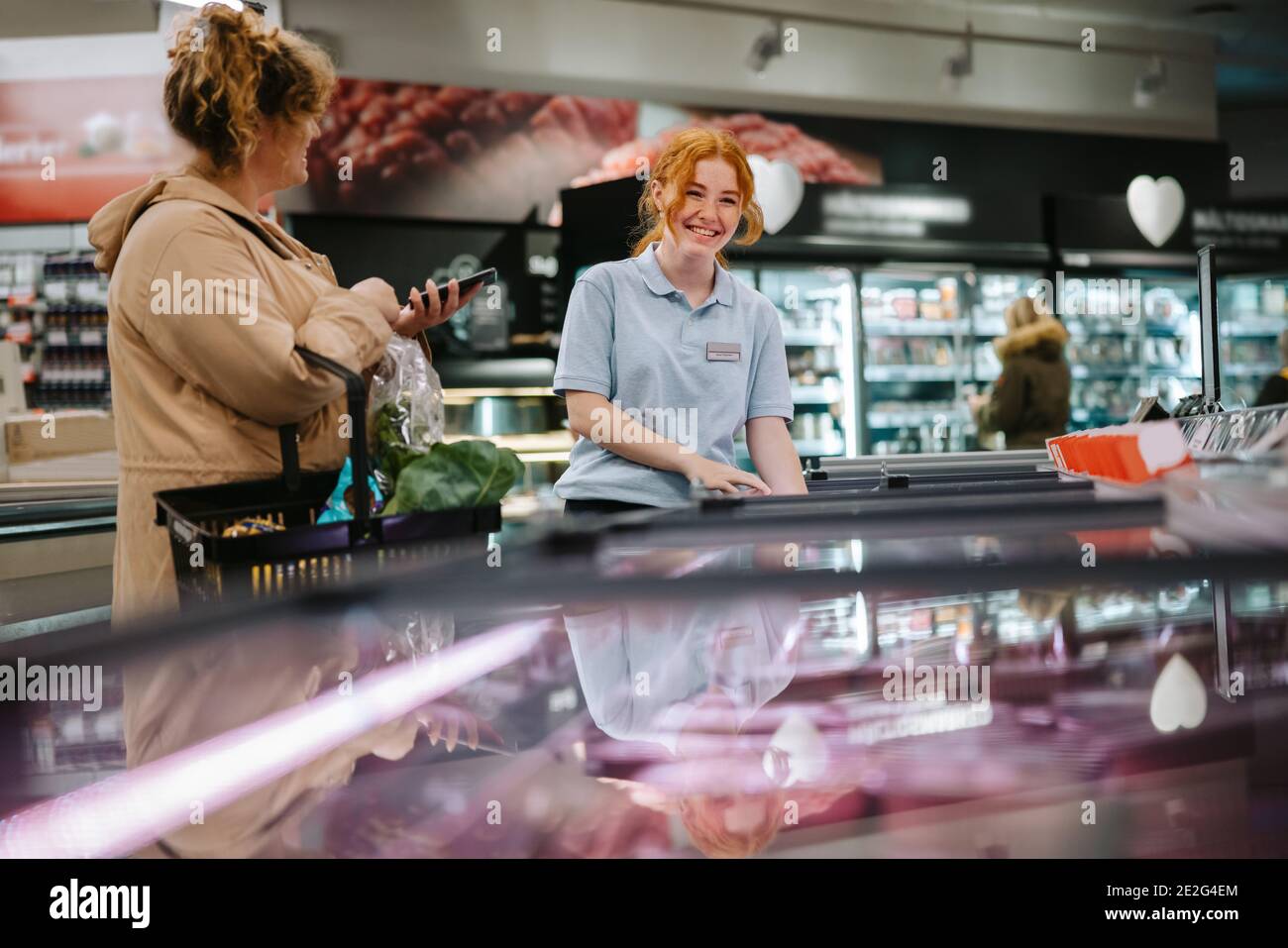 Un supermarket sorridente che aiuta il cliente in negozio. Acquirente ottenere aiuto da un giovane lavoratore in negozio di alimentari. Foto Stock
