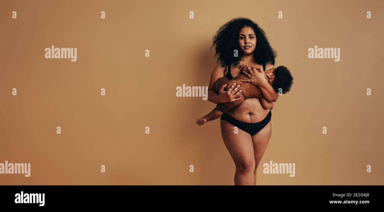 Madre africana che allatta il suo bambino. Donna e bambino postpartum in piedi su sfondo marrone. Foto Stock
