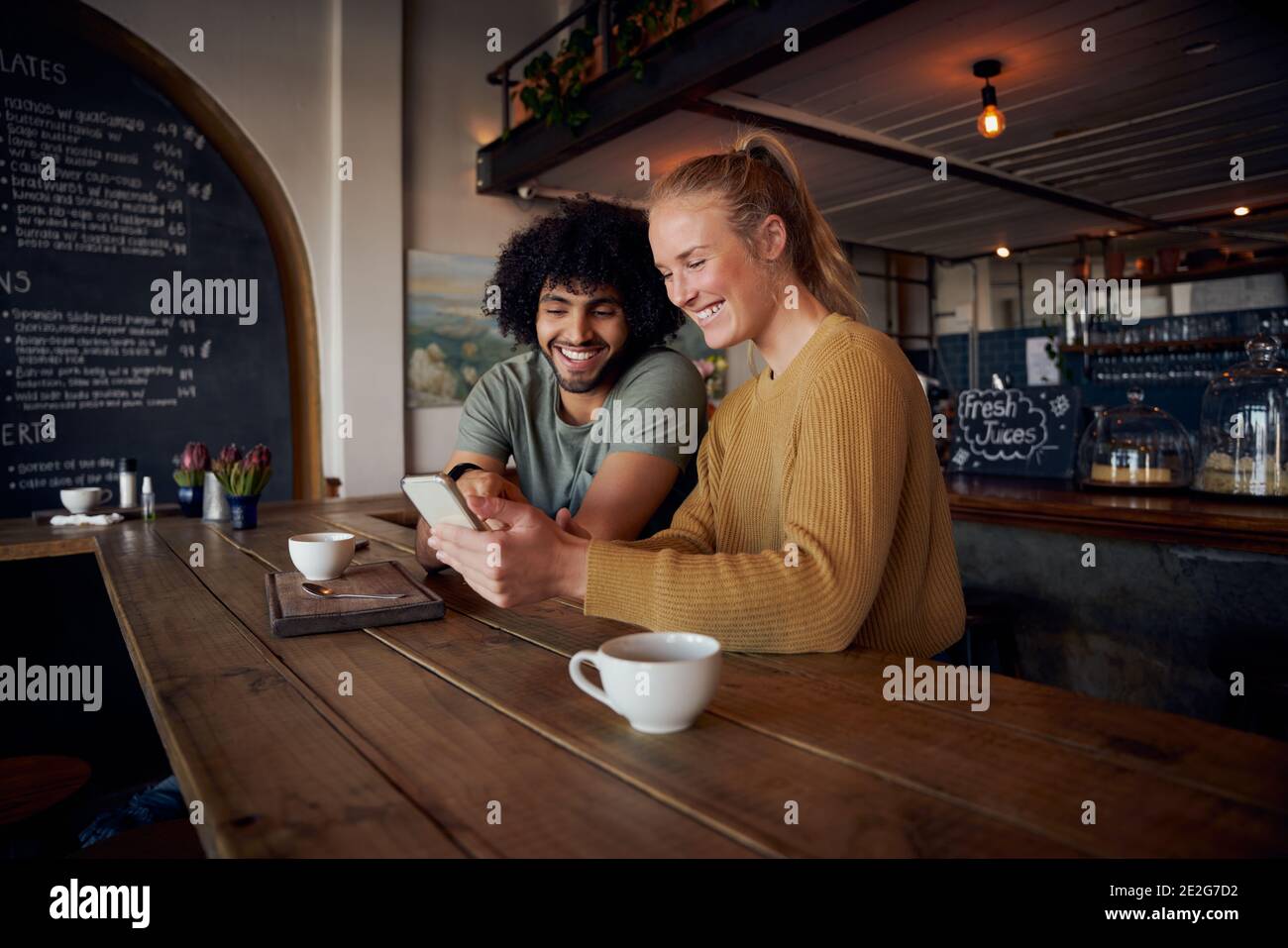 Una coppia sorridente che guarda lo smartphone seduto in un moderno caffè Foto Stock