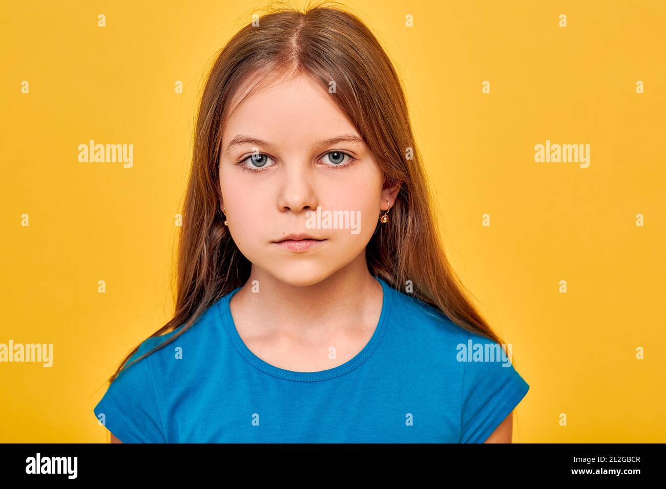 Bambina che indossa una t-shirt blu, etnia caucasica, serio e guardando la macchina fotografica, su sfondo oro fortuna Foto Stock