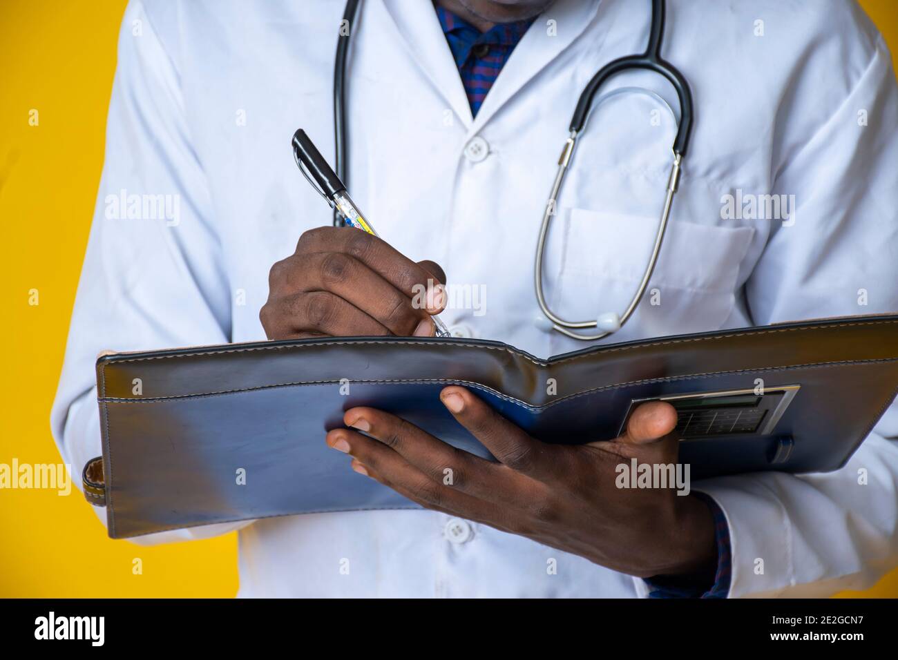 giovane bel medico nero che indossa il suo camice da laboratorio e. appendendo il suo stetoscopio sul collo e prendendo nota un blocco note Foto Stock