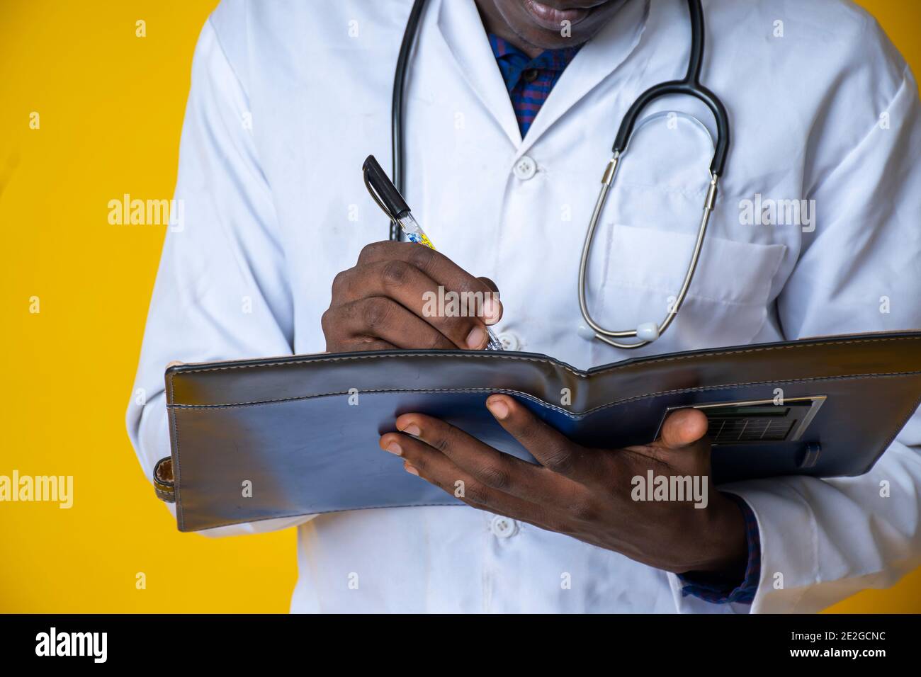 giovane bel medico nero che indossa il suo camice da laboratorio e. appendendo il suo stetoscopio sul collo e prendendo nota un blocco note Foto Stock