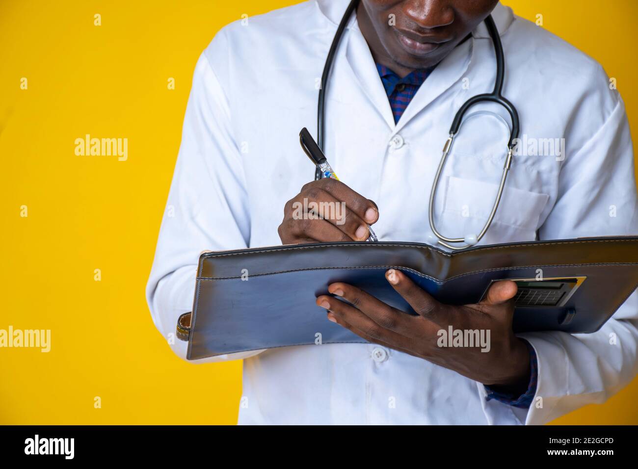 giovane bel medico nero che indossa il suo camice da laboratorio e. appendendo il suo stetoscopio sul collo e prendendo nota un blocco note Foto Stock