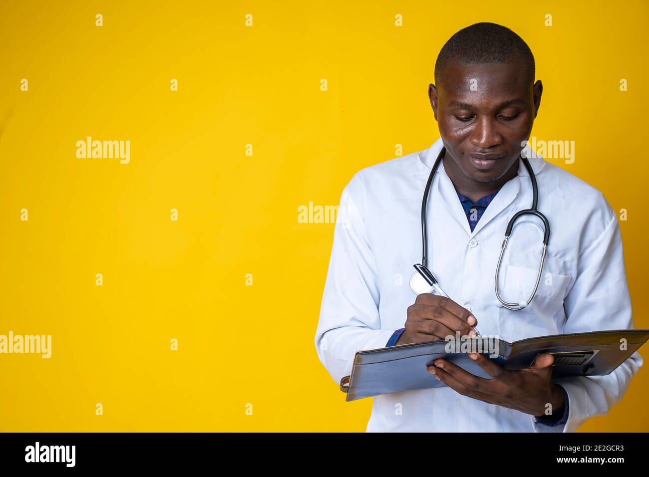 giovane bel medico nero che indossa il suo camice da laboratorio e. appendendo il suo stetoscopio sul collo e prendendo nota un blocco note Foto Stock