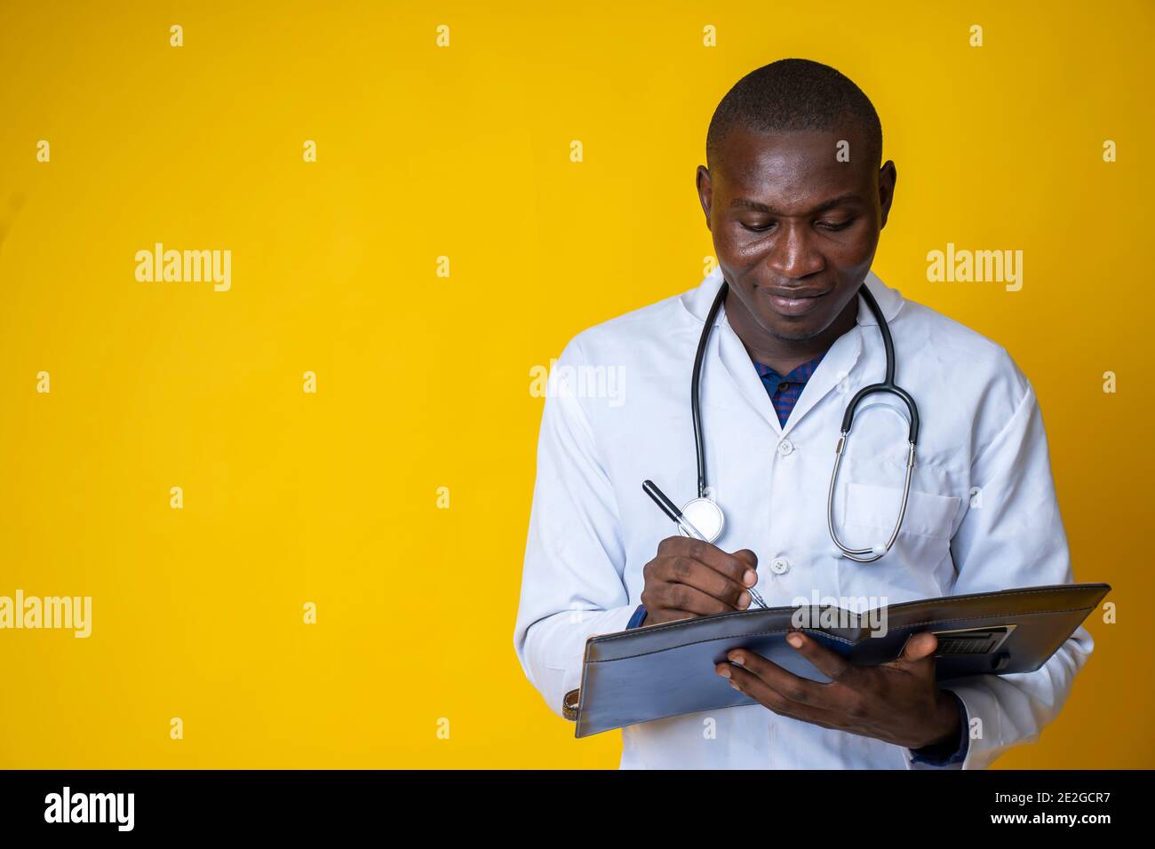 giovane bel medico nero che indossa il suo camice da laboratorio e. appendendo il suo stetoscopio sul collo e prendendo nota un blocco note Foto Stock