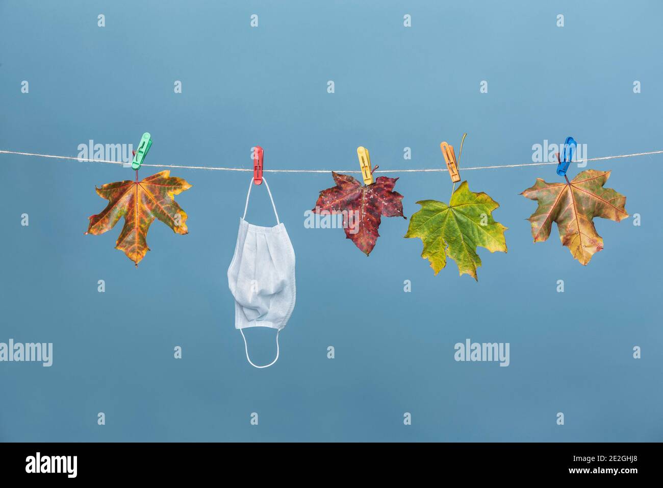 Maschera facciale appesa su stendiabiti con foglie autunnali Foto Stock