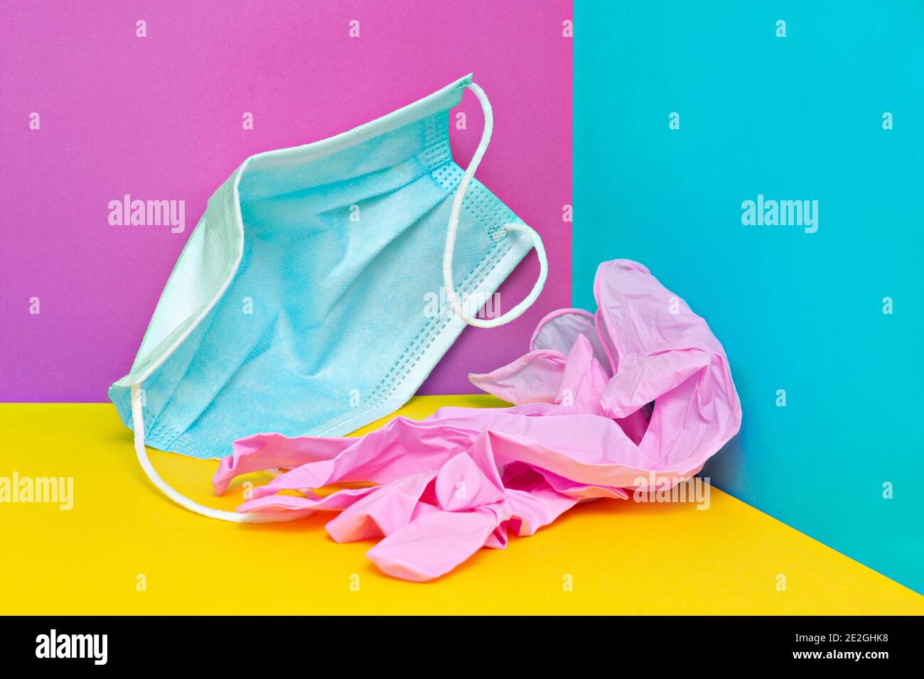 Maschera e guanti di plastica sgualciti su sfondo colorato Foto Stock