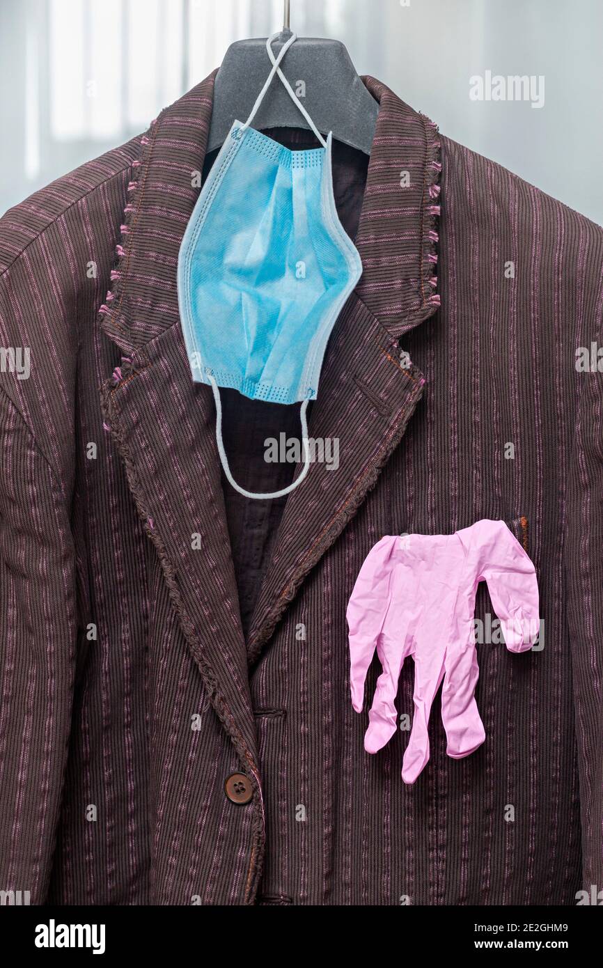 Maschera protettiva per il viso e guanti appesi alla giacca Foto Stock