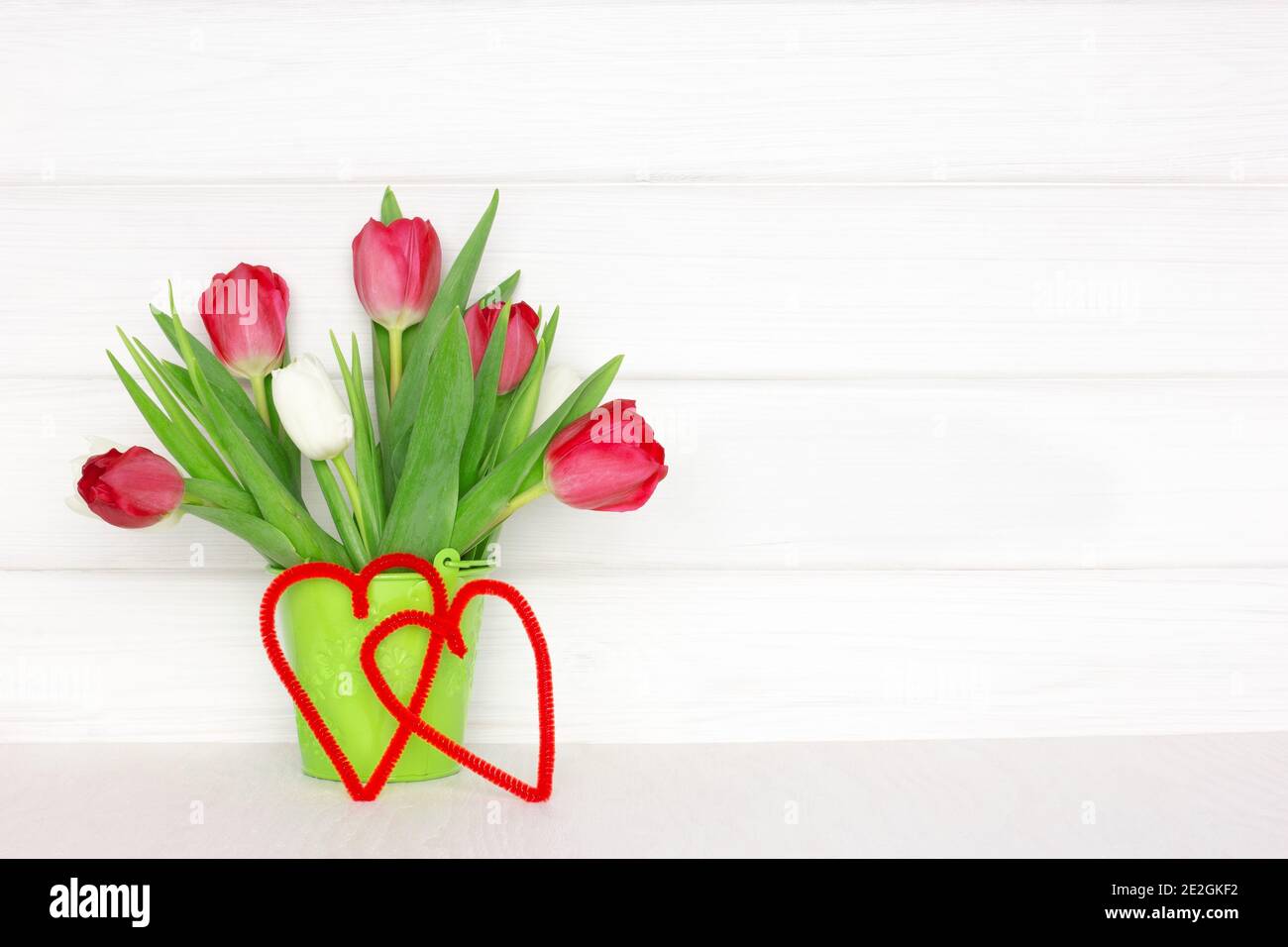 Bouquet di fiori tulipani con due cuori su un tavolo di legno vicino a parete di legno bianco. Concetto di San Valentino con spazio di copia. Primavera rustico sfondo Foto Stock
