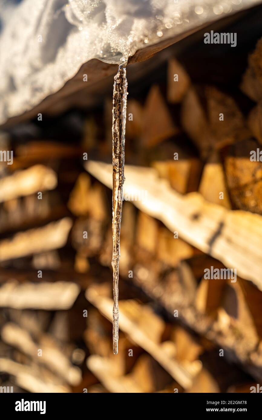 Holzstapel mit verschneitem Dach und Eiszapfen daran. Pila di legna da ardere con un tetto innevato e ghiaccio su di esso. Paesaggio alla luce del mattino Foto Stock
