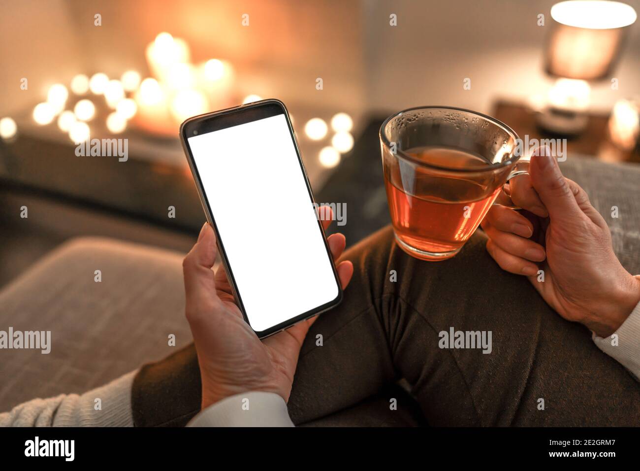 Nuova tecnologia di lettura che utilizza lo smartphone per apprezzare l'ebook preferito: Primo piano di una donna irriconoscibile seduta sul divano che tiene una tazza di tè in una mano Foto Stock