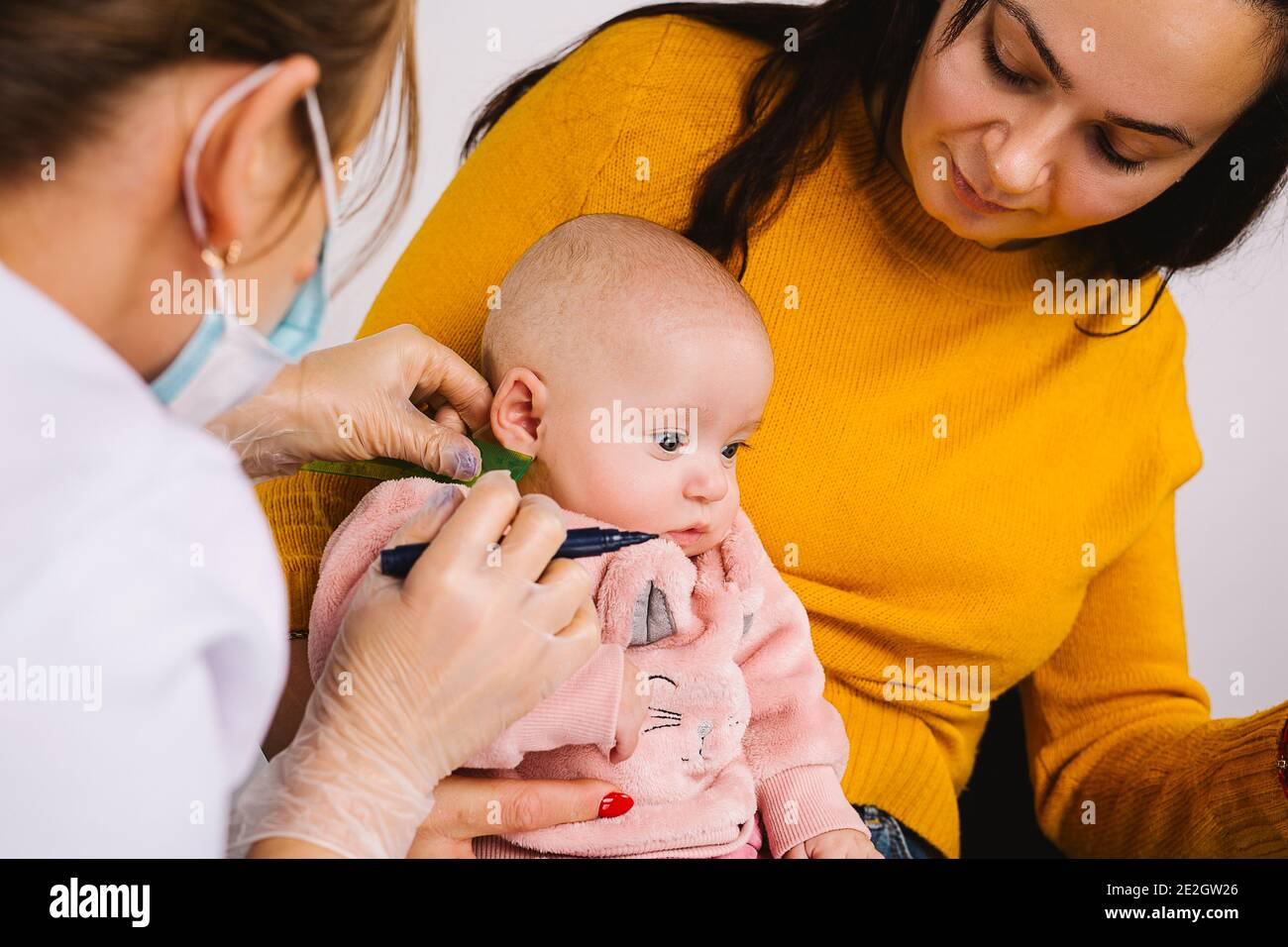 Foto ingrandita di una bambina il cui medico indica il posto per gli orecchini medici. Piercing dell'orecchio per i bambini. Foto ritagliata Foto Stock