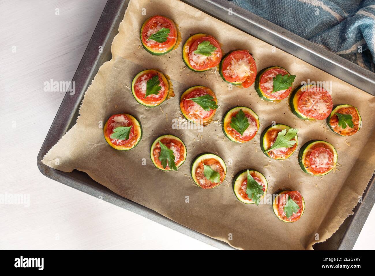 Fette di zucchine cotte al forno con pomodoro, formaggio e prezzemolo guarnire su una teglia da forno, spazio copia, vista dall'alto Foto Stock