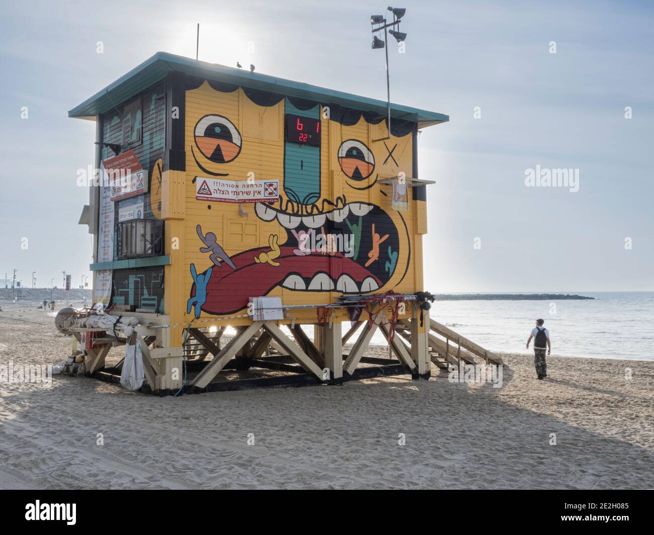 bella e divertente capanna bagnino con muro dipinto e un uomo in piedi sulla spiaggia di sabbia accanto ad esso. Foto Stock