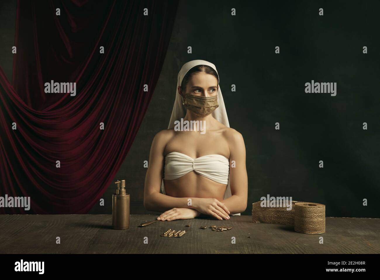 Assistenza sanitaria. Moderno remake di opere d'arte classiche con tema coronavirus - giovane donna medievale su sfondo scuro in posa con maschera dorata e pillole. Concetto di coronavirus, pandemia, creatività. Foto Stock