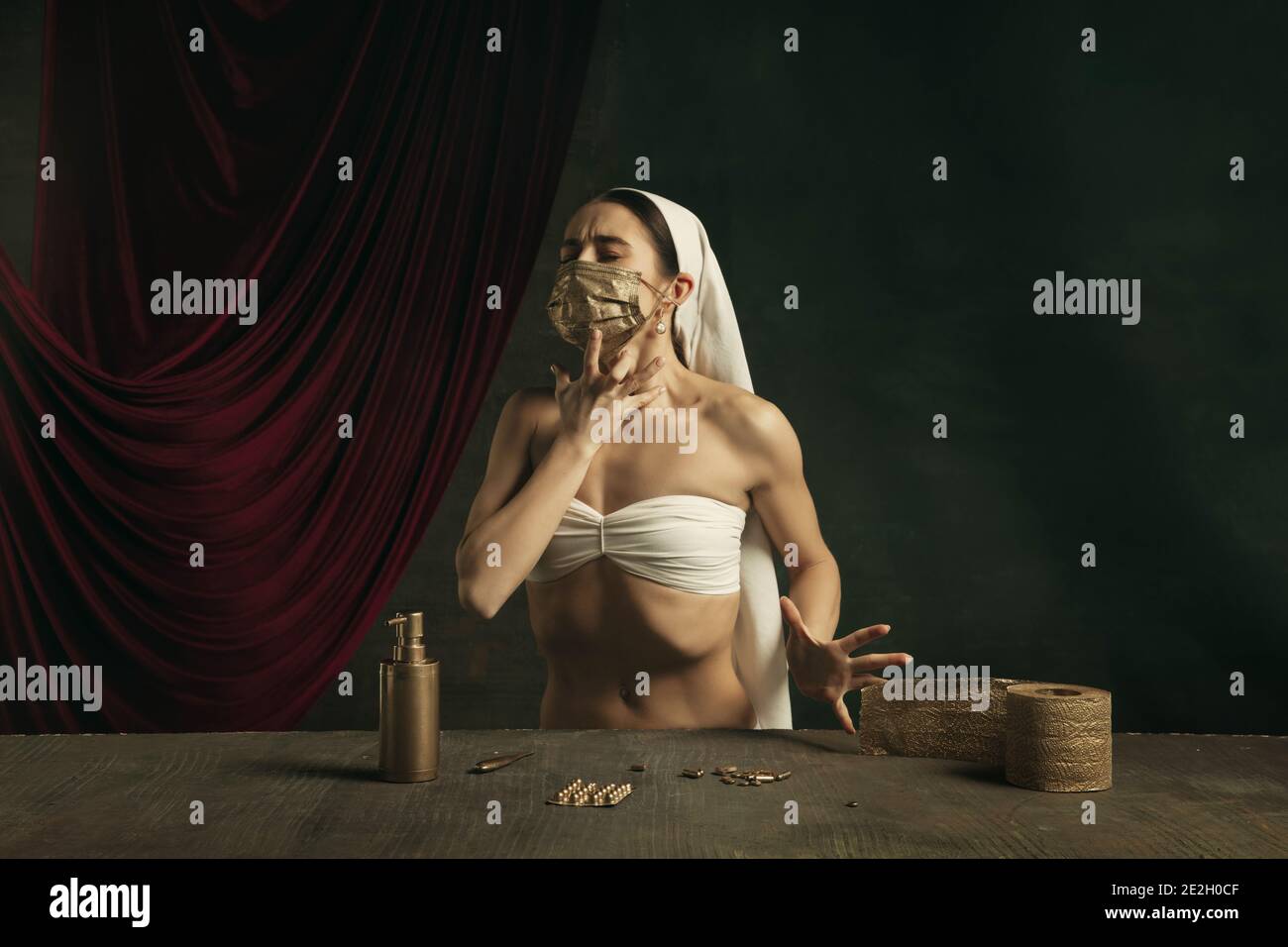 Assistenza sanitaria. Moderno remake di opere d'arte classiche con tema coronavirus - giovane donna medievale su sfondo scuro in posa con maschera dorata e pillole. Concetto di coronavirus, pandemia, creatività. Foto Stock