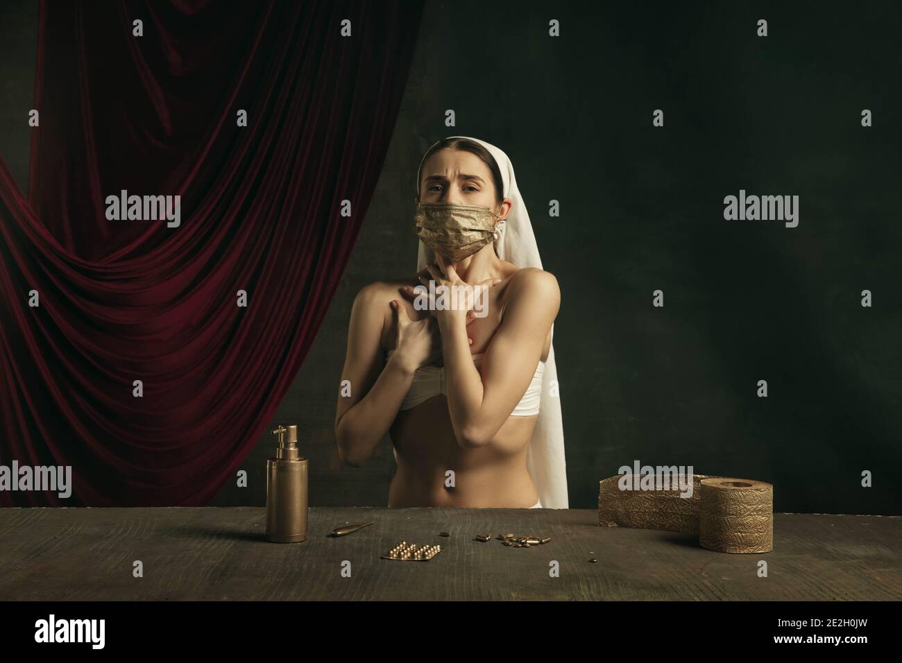 Assistenza sanitaria. Moderno remake di opere d'arte classiche con tema coronavirus - giovane donna medievale su sfondo scuro in posa con maschera dorata e pillole. Concetto di coronavirus, pandemia, creatività. Foto Stock