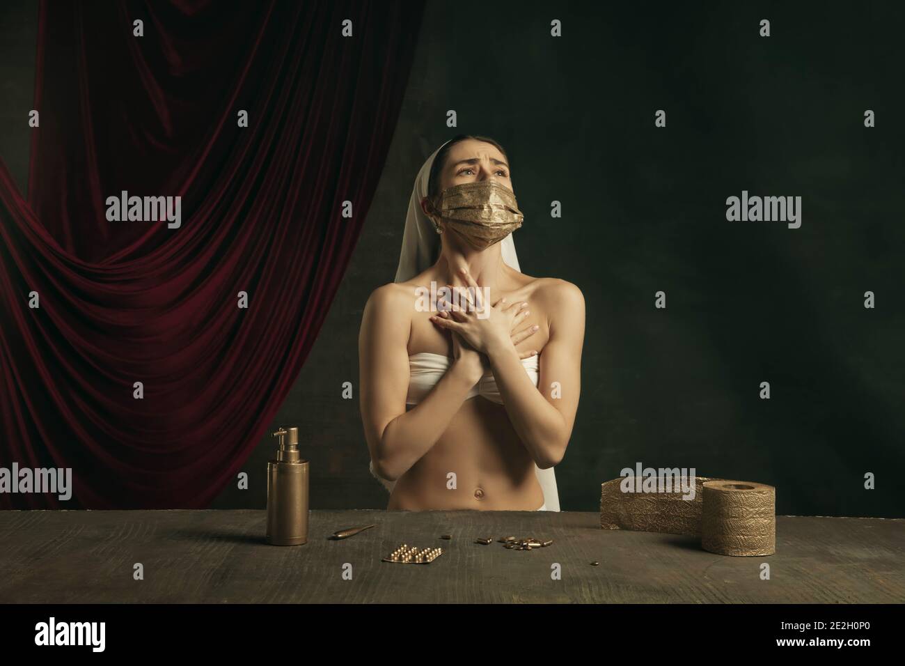 Respiro. Moderno remake di opere d'arte classiche con tema coronavirus - giovane donna medievale su sfondo scuro in posa con maschera dorata e pillole. Concetto di coronavirus, pandemia, creatività. Foto Stock
