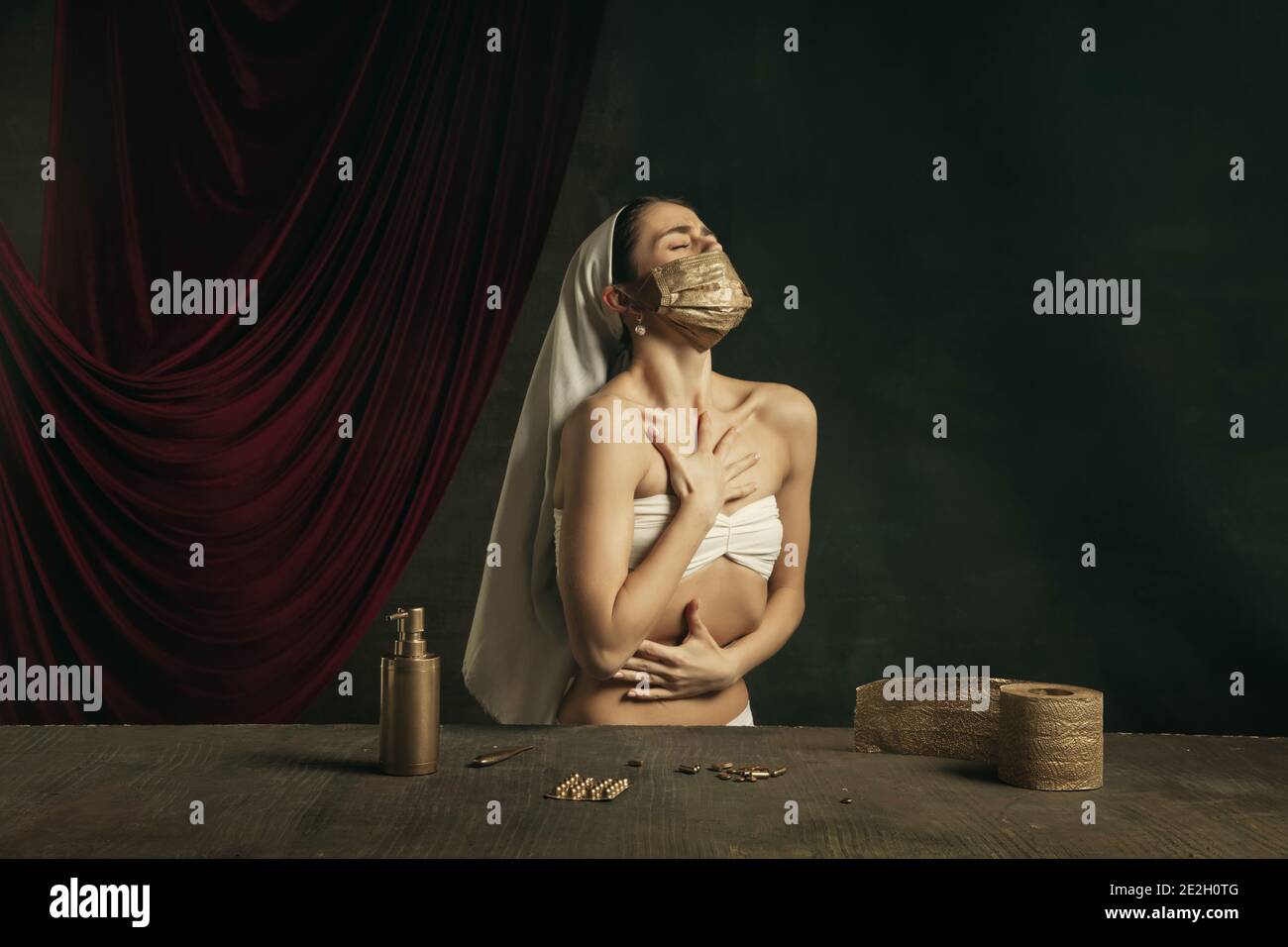 Respiro. Moderno remake di opere d'arte classiche con tema coronavirus - giovane donna medievale su sfondo scuro in posa con maschera dorata e pillole. Concetto di coronavirus, pandemia, creatività. Foto Stock