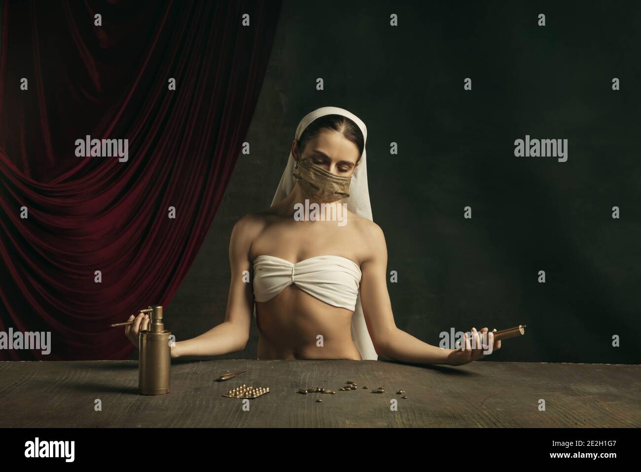 Medico. Moderna remake di opere d'arte classiche con tema coronavirus - giovane donna medievale su sfondo scuro in posa con maschera dorata e medicina. Concetto di coronavirus, pandemia, creatività. Foto Stock