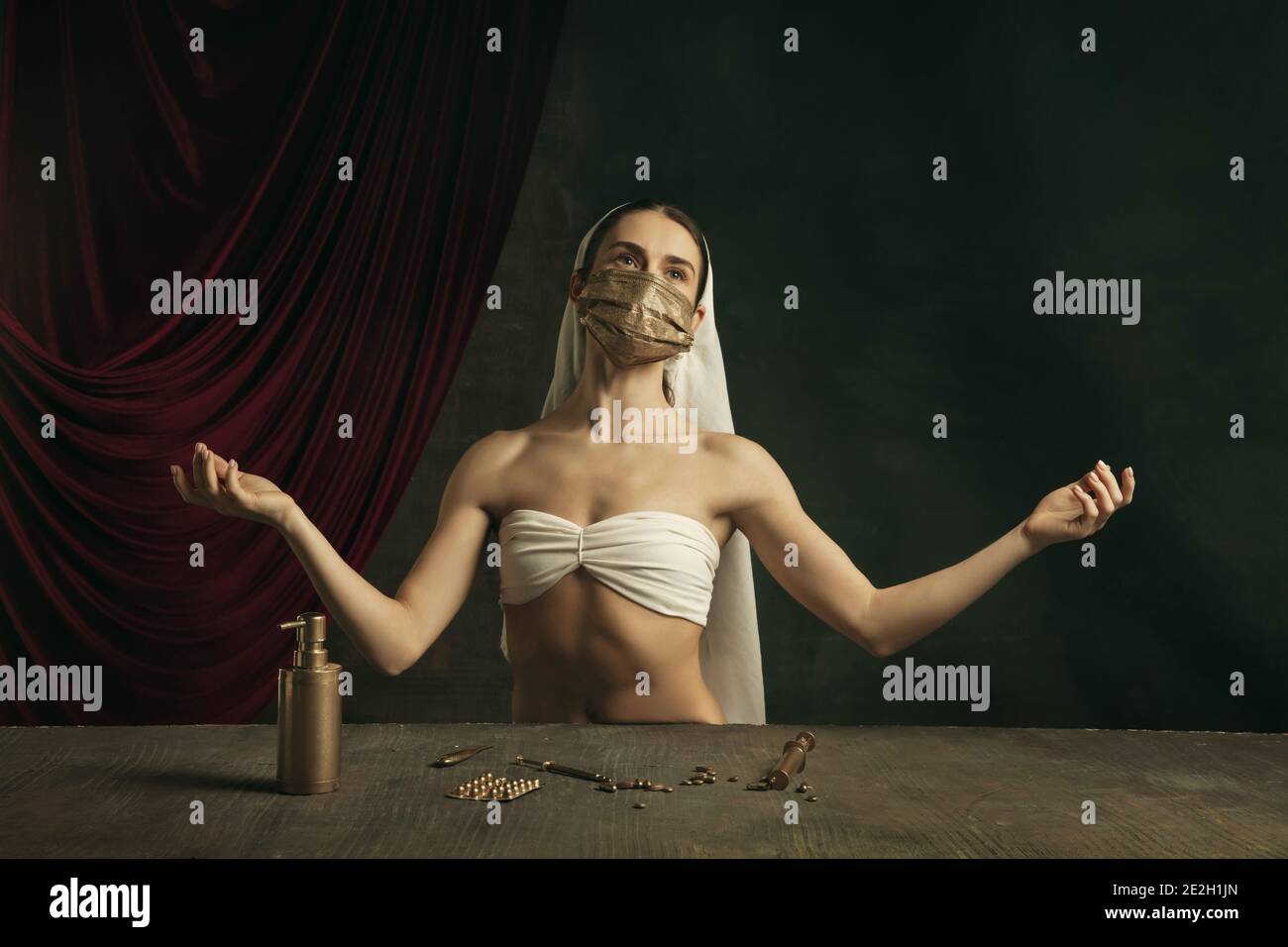 Medico. Moderna remake di opere d'arte classiche con tema coronavirus - giovane donna medievale su sfondo scuro in posa con maschera dorata e medicina. Concetto di coronavirus, pandemia, creatività. Foto Stock