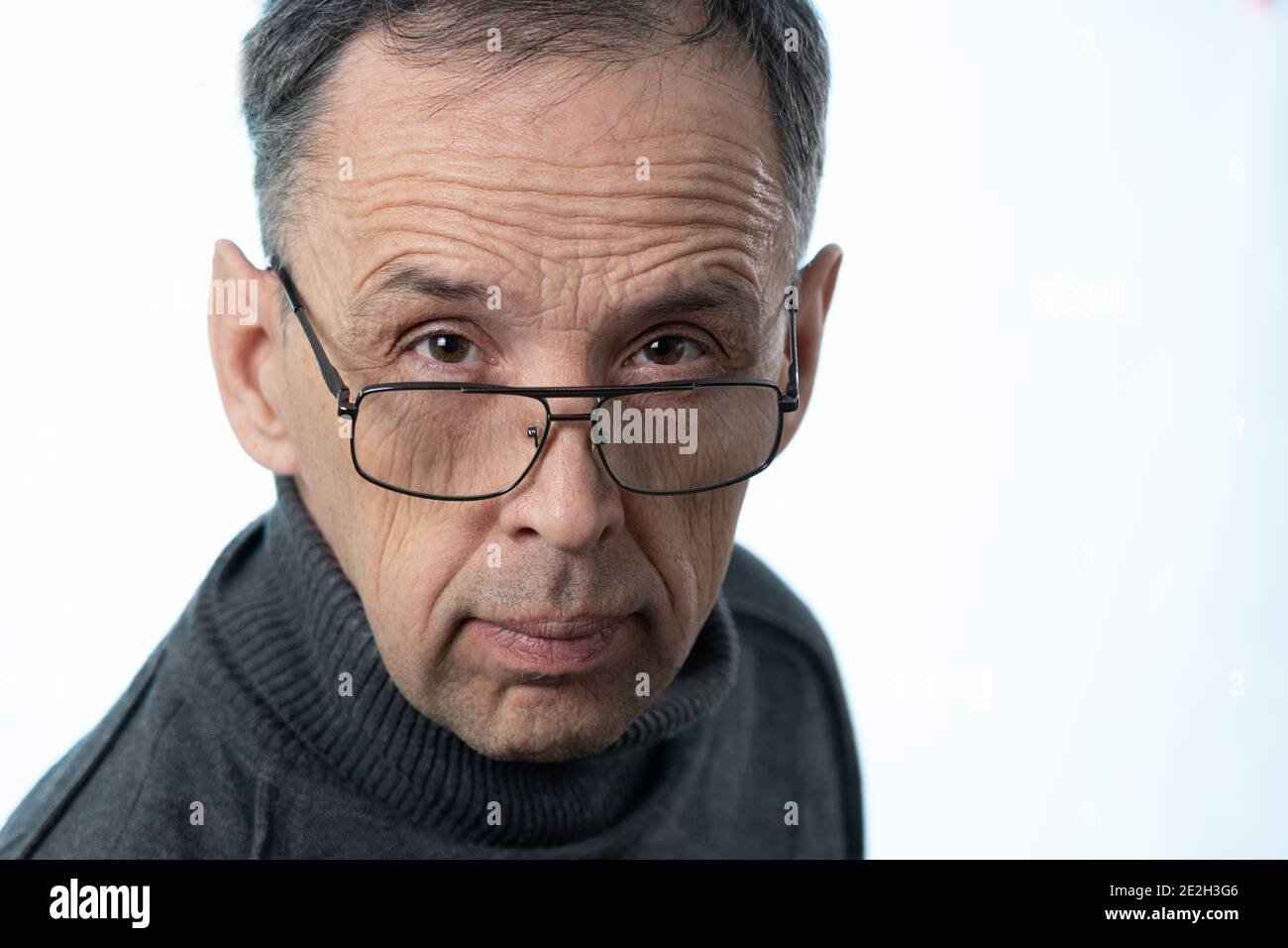 Un uomo anziano con un volto rugato guarda la fotocamera sopra i suoi occhiali. Ritratto di un pensionato russo su sfondo bianco in Studio. Foto Stock