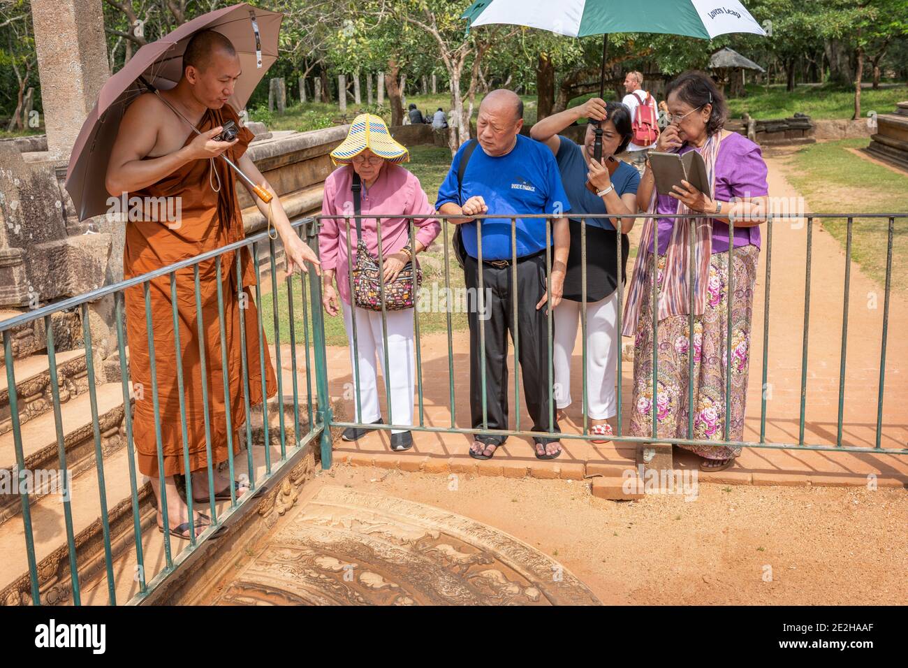 I turisti cinesi ascoltano come un monaco buddista spiega il significato Della 'pietra di luna' in un tour guidato dell'antica Sito di Polonnaruwa in Sri LAN Foto Stock