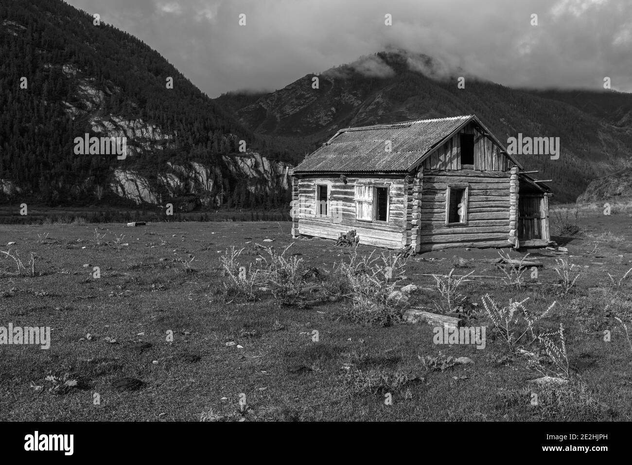 Bella fattoria retrò in legno abbandonato casa di tronchi senza finestre, sullo sfondo delle montagne Altai, cielo blu, estate, spazio copia, luogo per il testo, nero Foto Stock