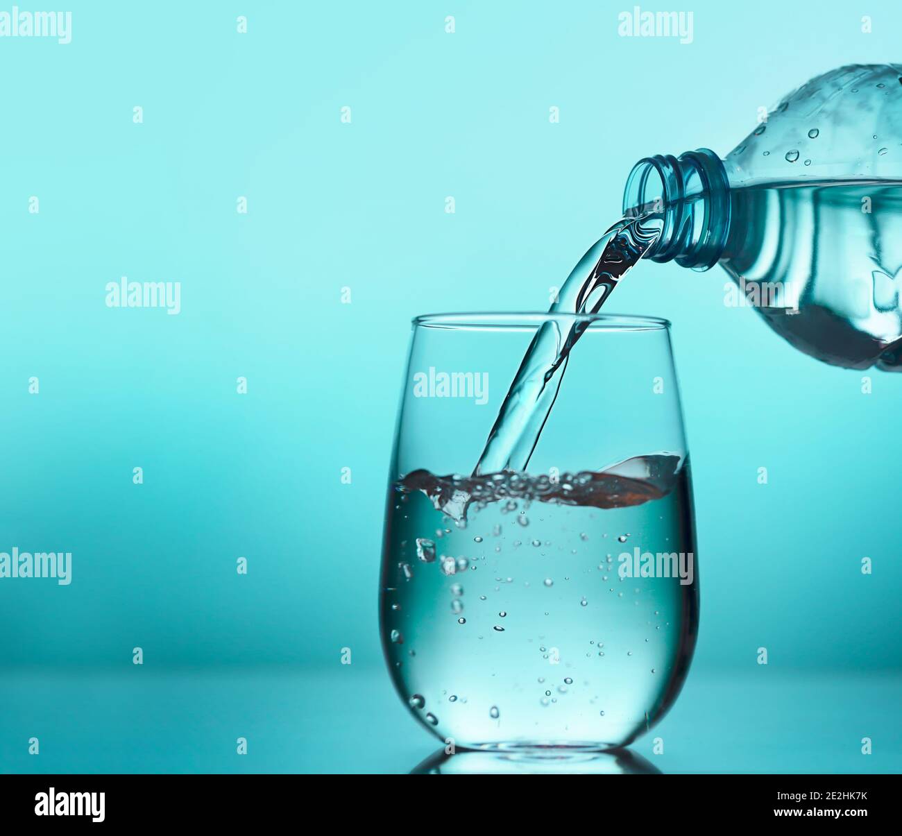 L'acqua fresca che viene versata dalla bottiglia di plastica in un bicchiere su sfondo blu. Bere acqua ogni giorno è importante per una salute ottimale Foto Stock