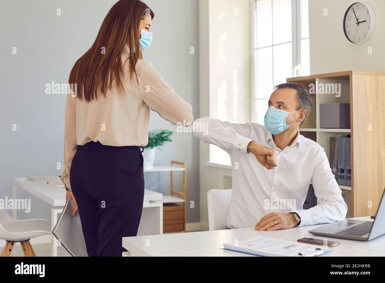 I colleghi in faccia ricoprono le maschere urtare i gomiti come alternativa alla normale stretta di mano Foto Stock