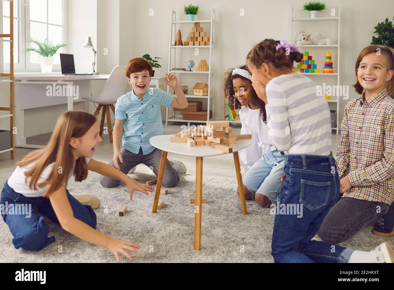 Gruppo di bambini che ridono alla torre di legno rotto mentre giocare gioco di tavolo impilato insieme Foto Stock