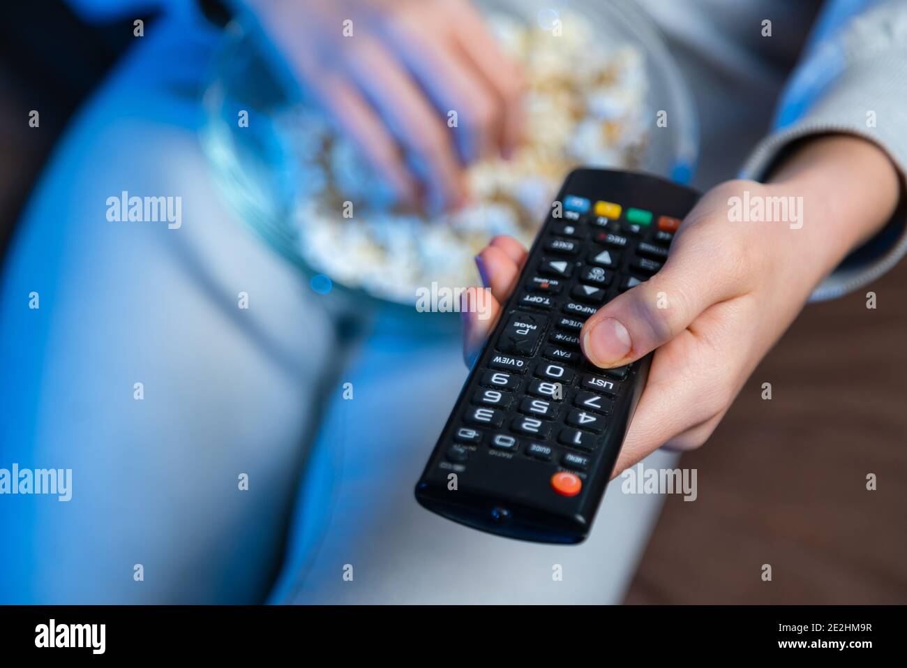 Primo piano del canale TV a commutazione manuale. La persona si siede in un comodo divano, mangia popcorn e guarda l'Home Cinema al buio. Foto Stock