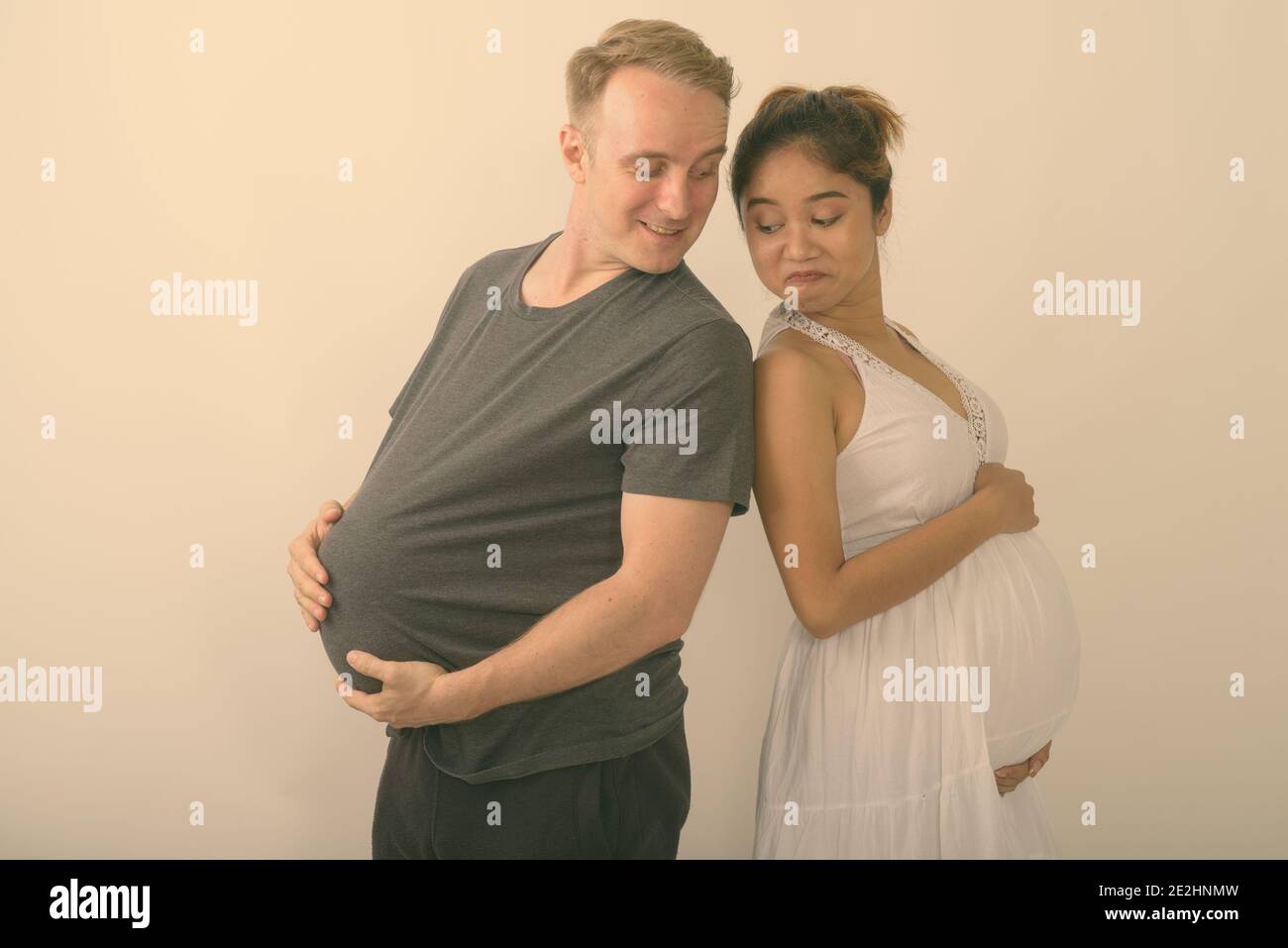 Studio shot di giovani felici multi-etnico coppia sposata sorridente guardando lo stomaco di ogni altra contro uno sfondo bianco Foto Stock