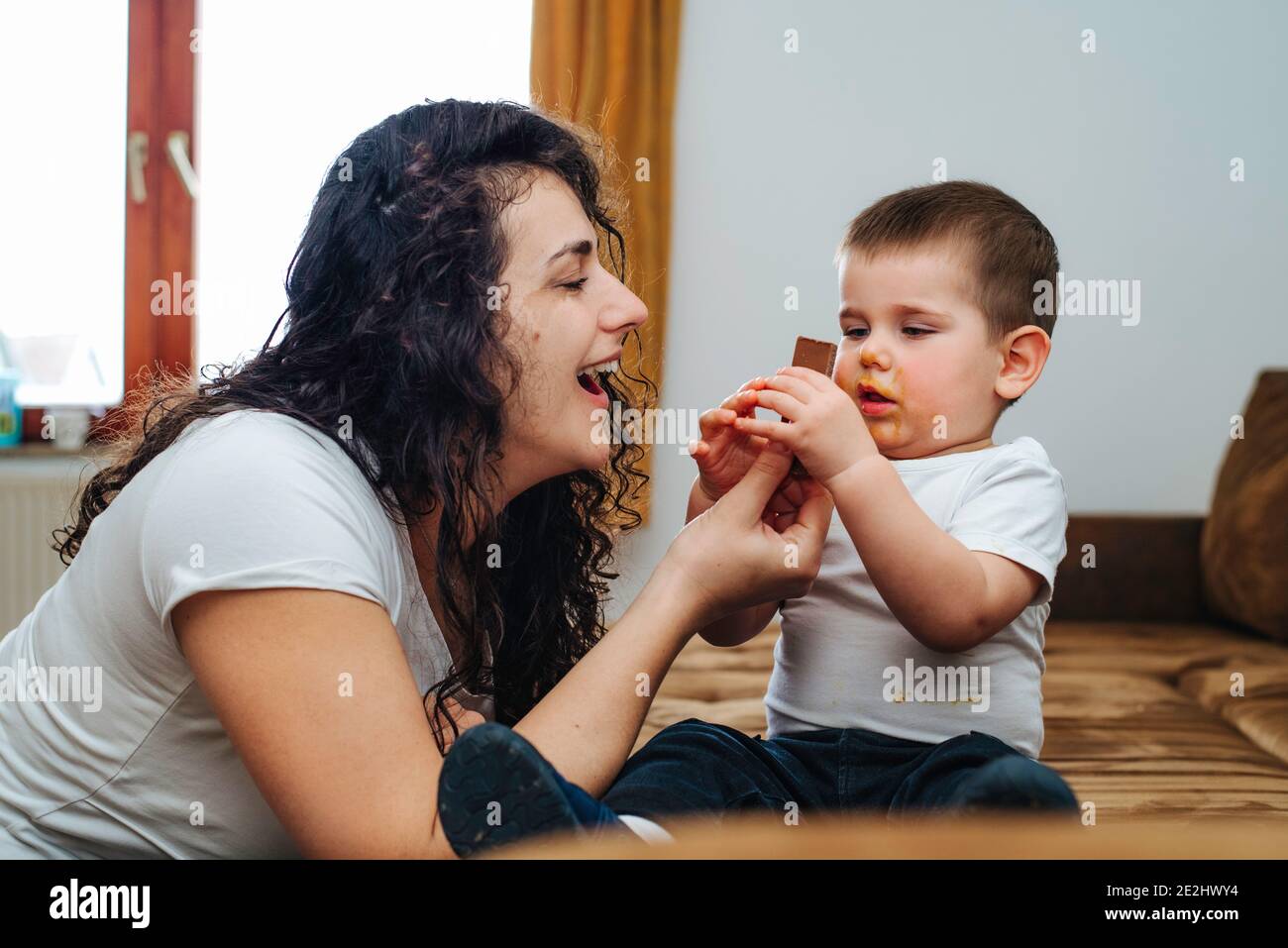 Ragazzo che mangia cioccolato mentre gioca con la mamma Foto Stock