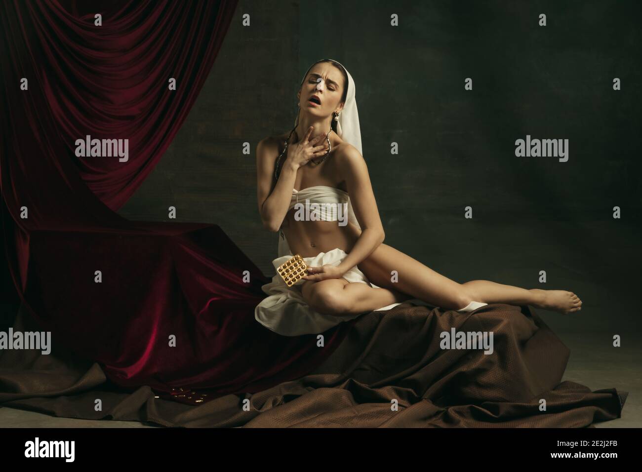 Trattamento. Moderna remake di opere d'arte classica con tema coronavirus - giovane donna medievale su sfondo scuro prendendo pillole di colore dorato. Concetto di coronavirus, pandemia, creatività, arte Foto Stock