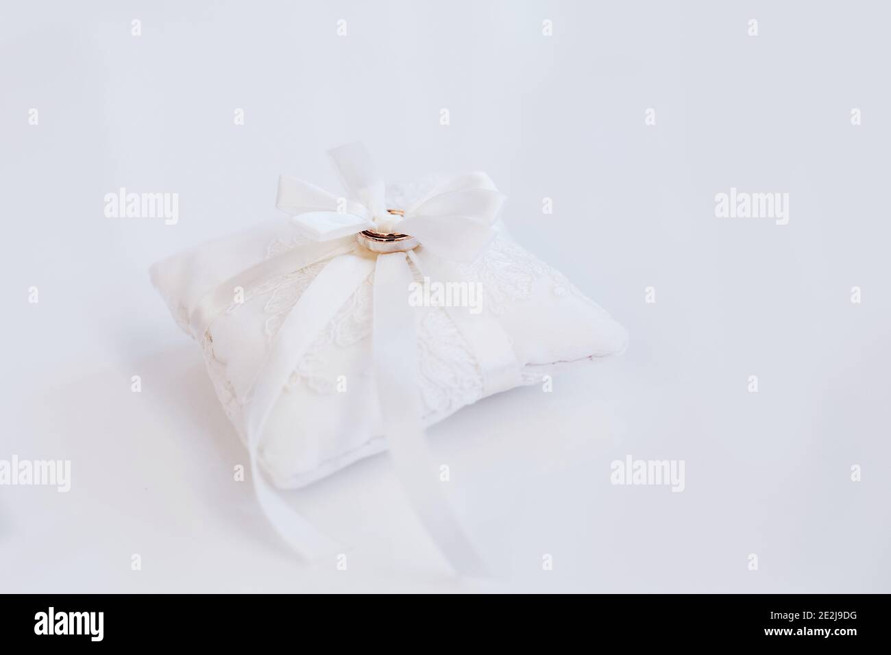 Due anelli di nozze d'impegno dorati su un piccolo cuscino d'arredo bianco cuscino con nastro Foto Stock