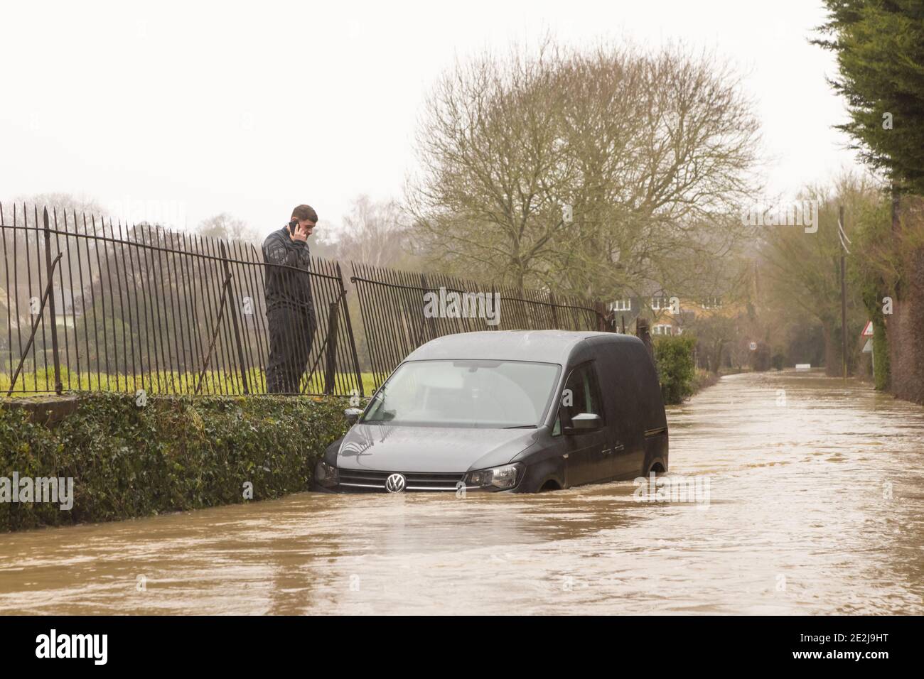 Uomo che telefona per aiuto dopo che il suo veicolo si è rotto in una strada allagata. Molto Hadham, Hertfordshire 14 gennaio 2021 Foto Stock